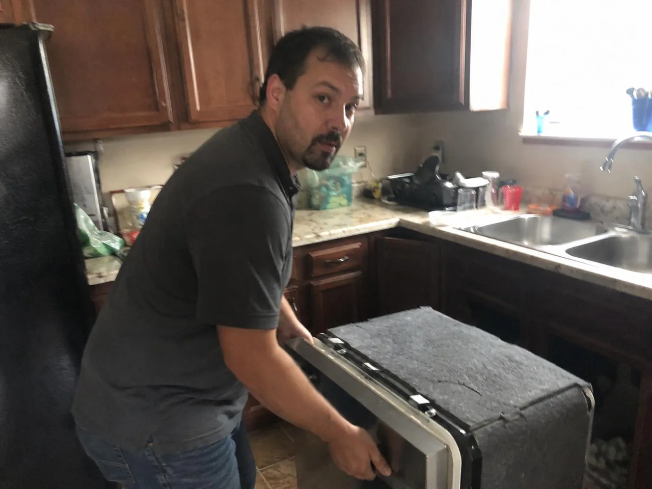 Technician handling a dishwasher during a repair visit